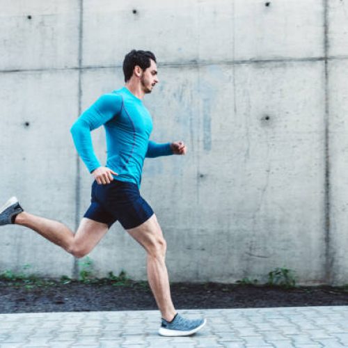 Side view of young man running outdoors in morning. Male athlete in running outfit sprinting outdoors.