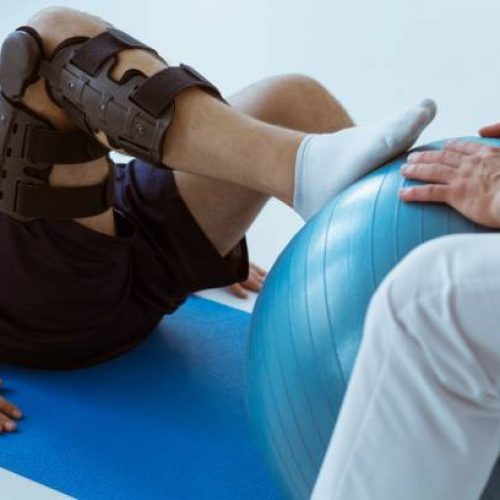 Pretty patient sitting on the blue mat in the gym and training with the ball