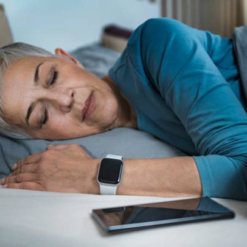 Sleep Apps - Tech-savvy Senior Woman Sleeping in Bed, Using Smart Phone and Smart Watch to Improve her Sleeping Habits